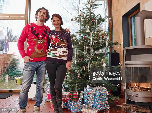 couple standing in front of christmas tree wearing christmas jumpers - christmas sweater bildbanksfoton och bilder