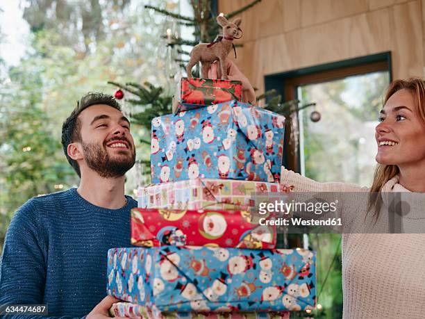 man carrying stack of christmas presents, woman putting reindeer on top - gift lounge stock-fotos und bilder