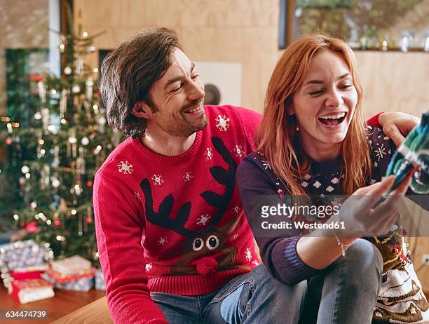 happy couple unwrapping children's shoes in front of christmas tree - sala di lusso foto e immagini stock