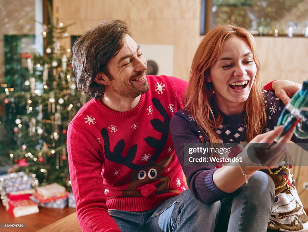 Happy couple unwrapping children's shoes in front of Christmas tree
