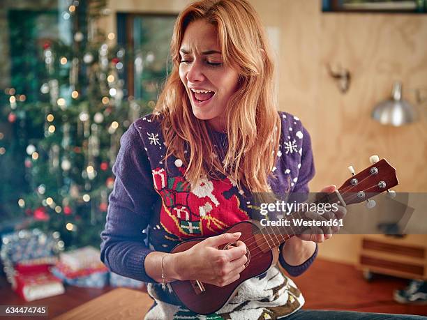 blond woman playing ukulele in front of christmas tree - christmas tree photos et images de collection