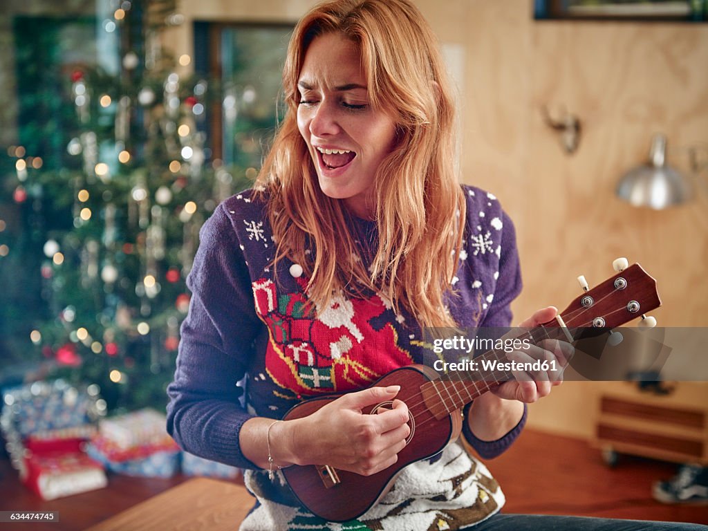 Blond woman playing ukulele in front of Christmas tree