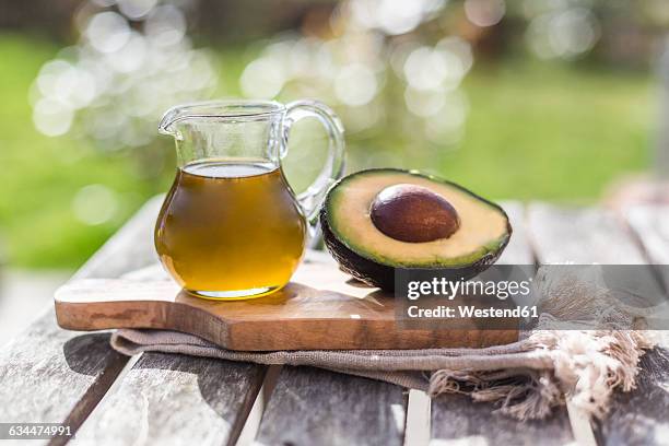 half of avocado and glass jug of avocado oil on wooden board - avocato oil stock-fotos und bilder