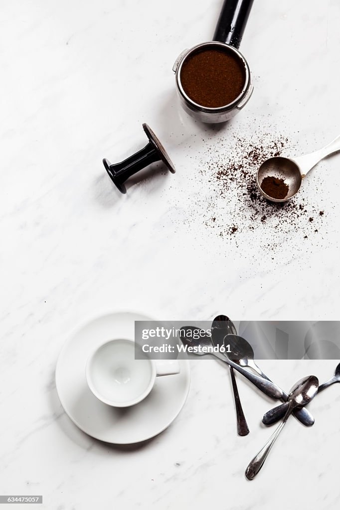 Empty espresso cup, spoons and pressurized portafilter on white marble