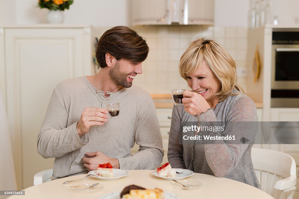 Mother and adult son drinking espresso in the kitchen and having fun together