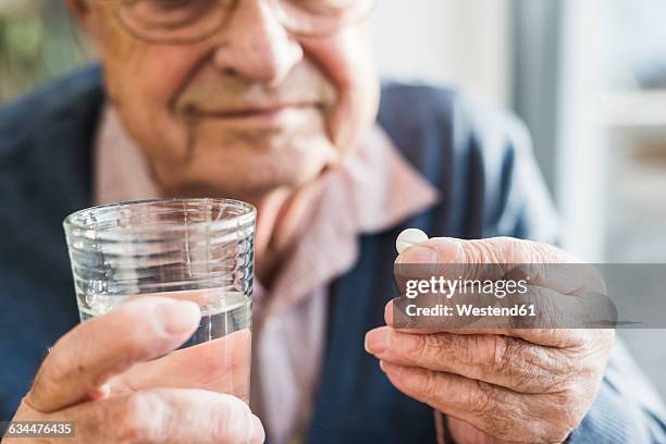 hands of senior man holding tablet and glass of water, close up - adults and pills stock-fotos und bilder