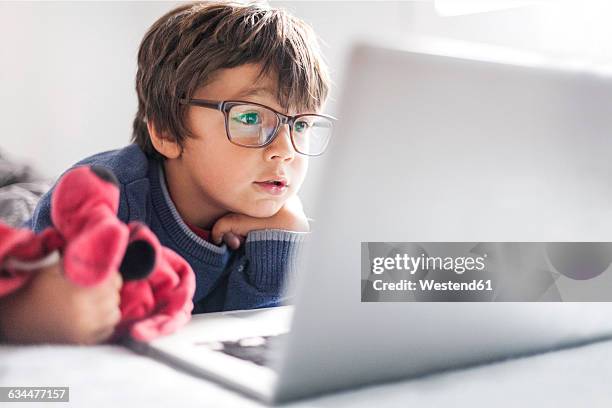 portrait of little boy wearing oversized glasses looking at laptop - kids eyeglasses stock pictures, royalty-free photos & images