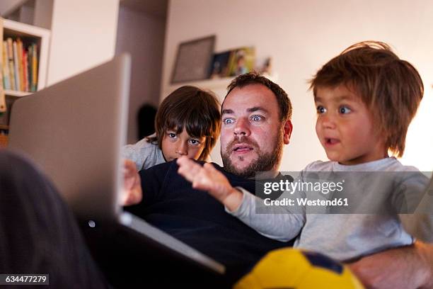 father and his two little sons looking video on the laptop at home - surfing the net stock pictures, royalty-free photos & images