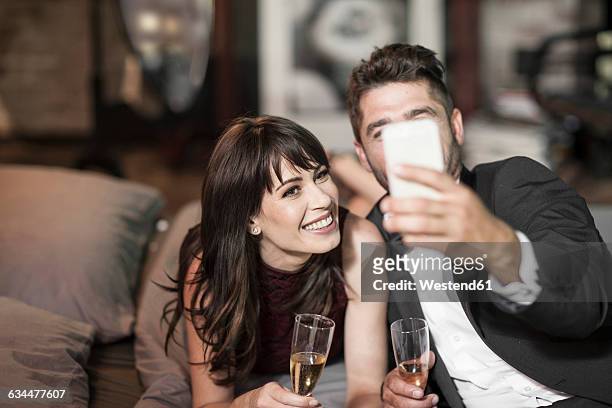 smiling couple in elegant clothing drinking champagne in bed and taking a selfie - obscured face phone stock pictures, royalty-free photos & images