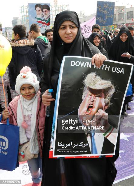 An Iranian woman holds a placard showing a caricature of US President Donald Trump being punched by a hand wearing a bracelet of the Iranian flag...
