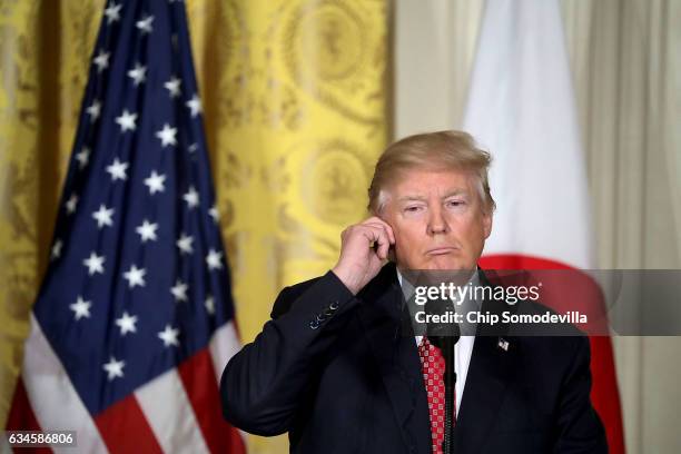 President Donald Trump uses an earbud to hear a translation of Japanese Prime Minister Shinzo Abe during a joint press conference in the East Room of...