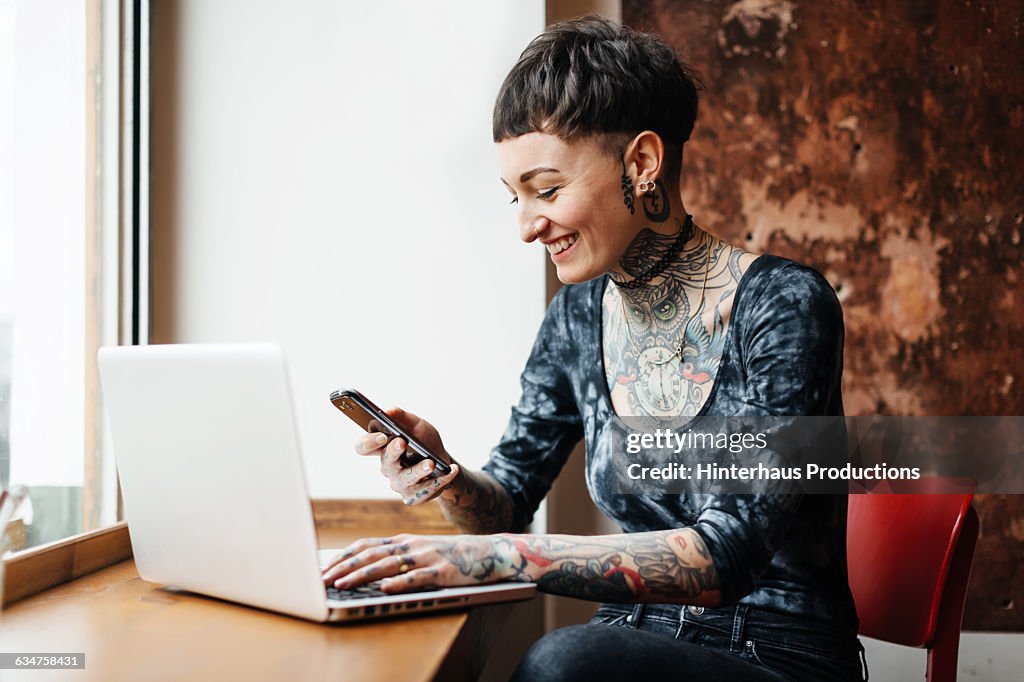 Young tattooed woman checking her phone in a café