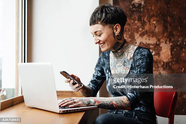 young tattooed woman checking her phone in a café - tatouage femme photos et images de collection