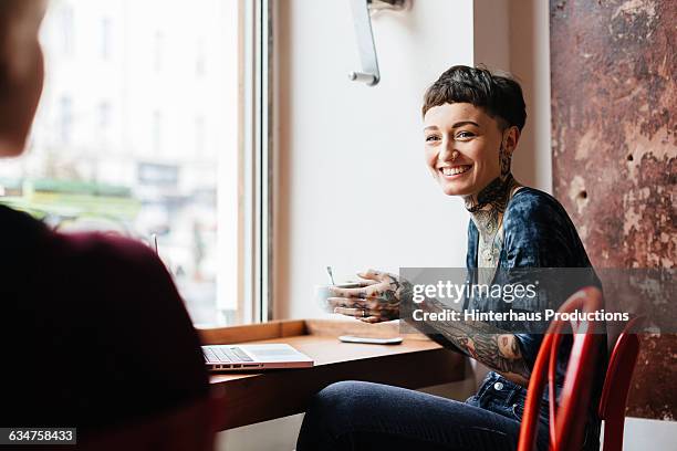 tattooed young woman having a cup of coffee. - schort fotografías e imágenes de stock