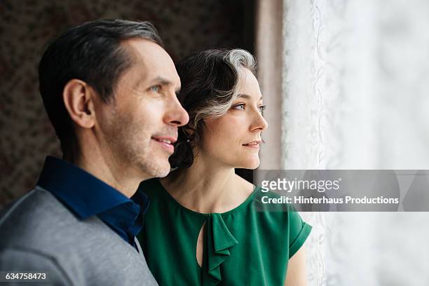 mature couple looking out of a big window. - blouse man stockfoto's en -beelden