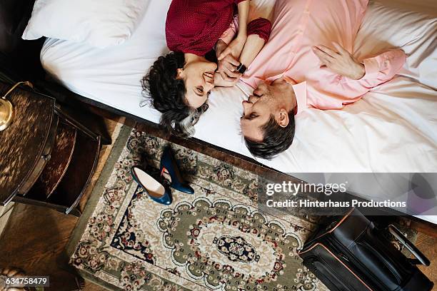 loving couple lying in hotel bed together - hotel room stock-fotos und bilder