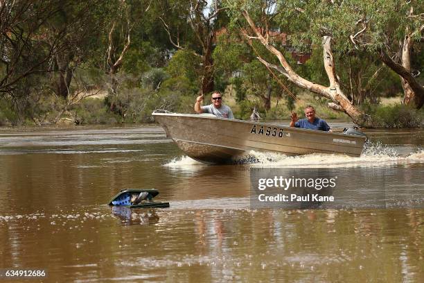 Two men in small boat wave to people on the bank while traversing across a flooded Middle Swan Reserve picnic area, as flood waters are seen in the...
