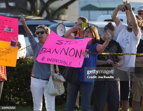 Protesters hold a sign that reads, " Stop Bannon," as they raise their their middle fingers as President Donald Trump passes by February 12, 2017 in...