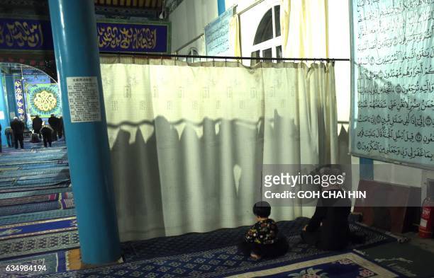 This picture taken on September 19, 2015 shows a Chinese Hui Muslim woman and her child praying behind a curtain during evening prayers at the Great...