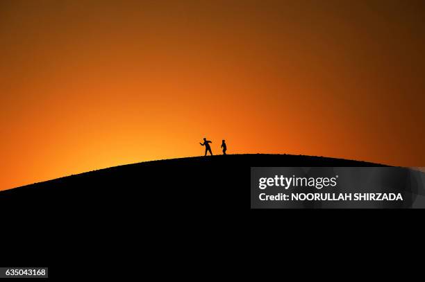 In this photograph taken on February 12 Afghan youth play on a hilltop as the sun sets on the outskirts of Jalalabad. / AFP PHOTO / NOORULLAH SHIRZADA