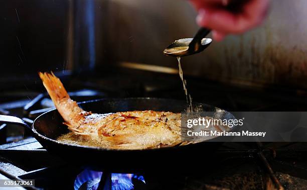 whole snapper being sauteed in a pan - fried stockfoto's en -beelden