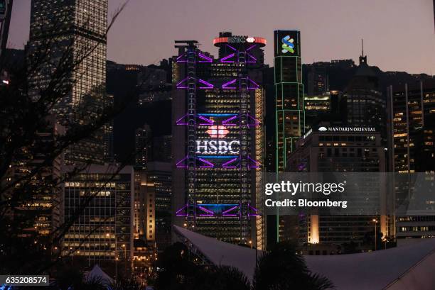 The HSBC Holdings Plc headquarters building, center, and the Standard Chartered Plc building, center right, stand illuminated at dusk in the Central...