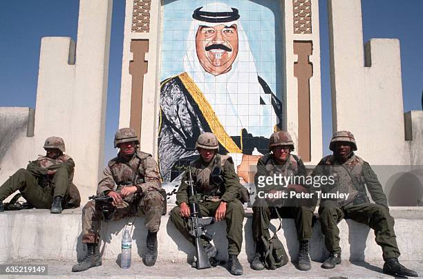 Soldiers fighting in the Gulf War sit under a portrait of Iraqi leader Saddam Hussein at the border of Iraq and Kuwait. | Location: Border of Iraq...
