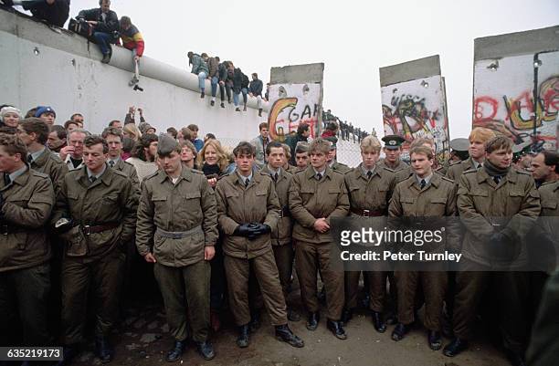 East German soldiers stand by as the Berlin Wall is dismantled, November 1989.