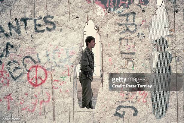 Two East German soldiers as seen through holes in the Berlin Wall, November 1989.