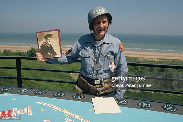Coast Guard veteran Charles Gifford holds a photo of himself 50 years before at commemorations of the D-Day invasion from an observation point at