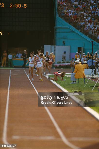South African runner Zola Budd watches her chief competitor, American Mary Decker, fall to the ground in the final of the Women's 3,000-meter run at...