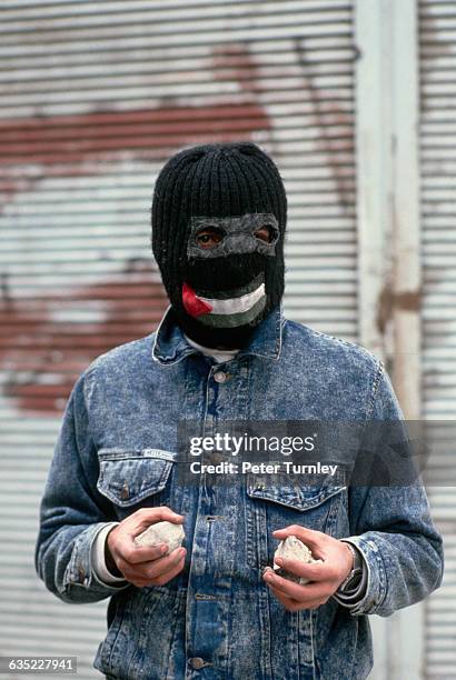 Young man wearing a ski mask with the Palestinian flag sewn over the mouth, holding rocks, during the Intifada.