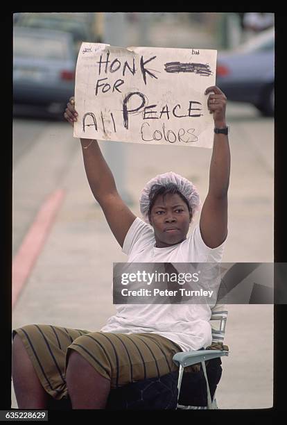 Woman holds a sign asking motorists of all races to honk their horns for peace during the riots which ensued after white Los Angeles police officers...