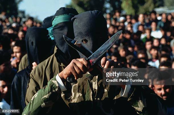 Palestinian guerilla wearing a mask over his face crosses two daggers at a Hamas rally in Gaza.