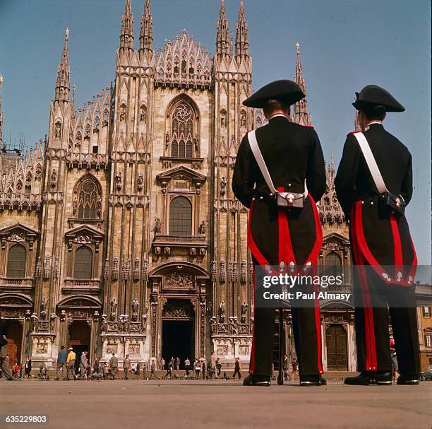 Two carabinieri in uniform stand watch in the Piazza del Duomo at Milan, Italy, under the facade of the city's great 14th-century cathedral.