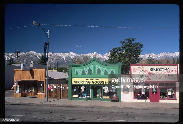 Storefronts of a bike shop and a sporting goods store, with the Sierra Nevada Mountains in the background. | Location: North of Bishop, California,...