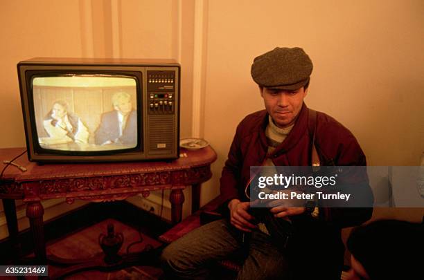 An amused armed rebel watches Nicolae Ceausescu's own office television set as it broadcasts a tape of the trial of Ceausescu and his wife Elena. The...