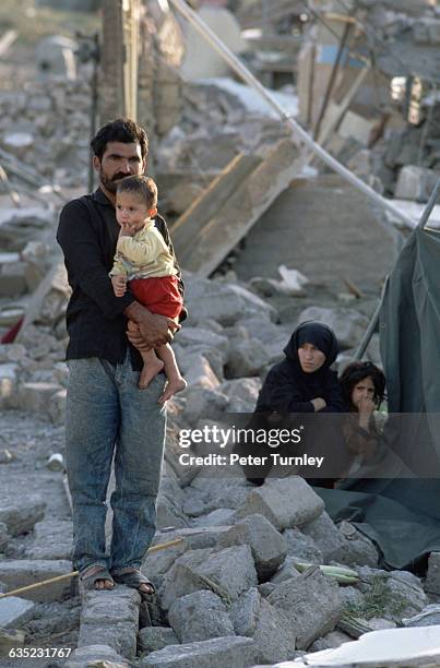 Father holding his young son stands among rubble. Their town was laid waste after being struck by a severe earthquake. Casualty estimates have...