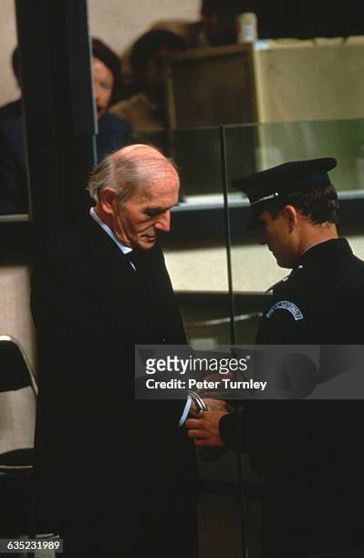 Police officer unlocks the handcuff on fugitive Nazi Klaus Barbie during his trial for crimes against humanity in Lyon, France.