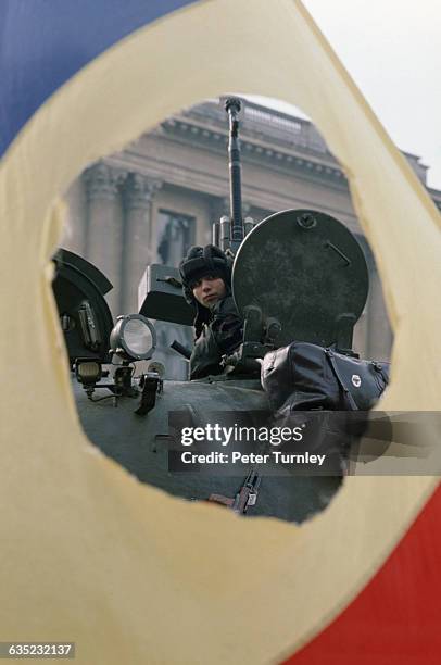 Romanian soldier mans his tank in Bucharest's Palace Square, seen through the hole in a Romanian flag where the Communist symbol used to be.