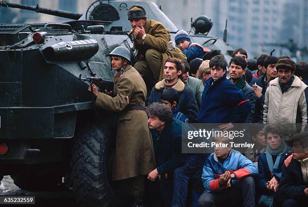 During the 1989 revolution, Romanian soldiers and civilians take cover behind a tank in Bucharest's Palace Square.