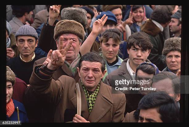 Avram Constantin of Bucharest weeps and flashes victory signs along with the gathered crowd on Christmas Day as he watches trucks go by bearing dead...