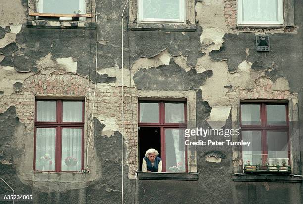 An elderly East German woman looks out the window of her dilapidated apartment.