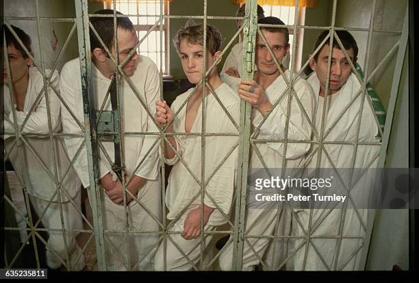 Mentally-ill patients stand behind the cell bars of their hospital room at a psychiatric ward. | Location: near Moscow, Russia.