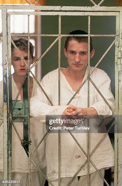 Mentally-ill patients stare from behind cell bars in their room at a psychiatric hospital. | Location: near Moscow, Russia.