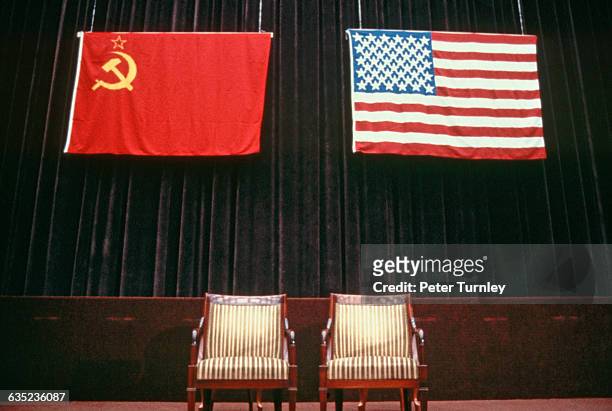 The flags of the USSR and USA hang over chairs on stage at the 1985 Geneva Summit.