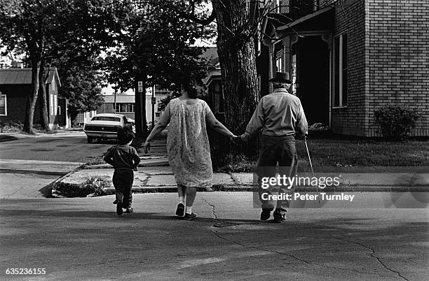 Blind Hispanic man crosses McClellan Street with his wife and son. Fort Wayne, Indiana.