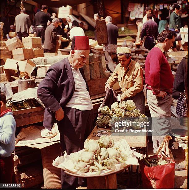 Elderly man in a red fez examines artichokes in a street market in Beirut, Lebanon, April 1967.