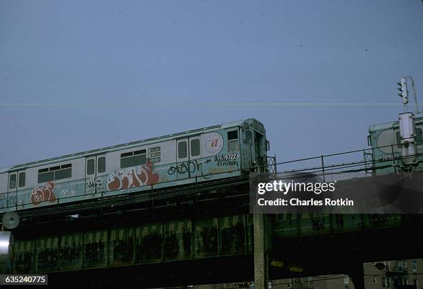 Subway car on an elevated railroad is covered with graffiti. New York City, August 1975.