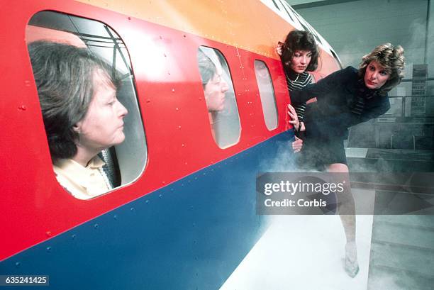 Flight crew aboard a United Boeing 767 flight simulator evacuate through a door over the wing as passengers look on through windows. The flight crew...